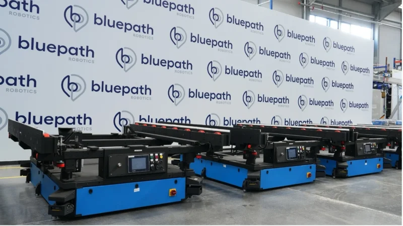 Factory interior view showing multiple Bluepath Robotics autonomous mobile robots aligned in production, representing industrial automation solutions.